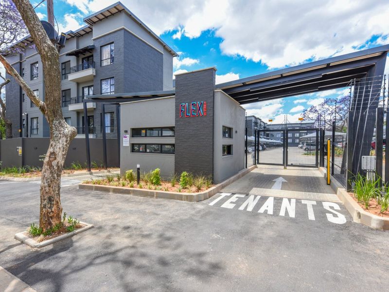 The main entrance to the apartment complex featuring a secure gated access point, guard house, and well-maintained paved driveway.