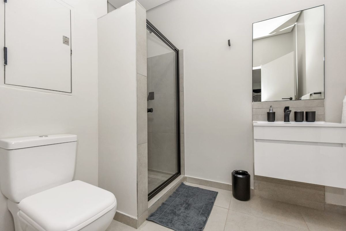 A modern, well-maintained bathroom featuring a glass-enclosed shower, a sleek white vanity with a basin, and contemporary black fixtures.