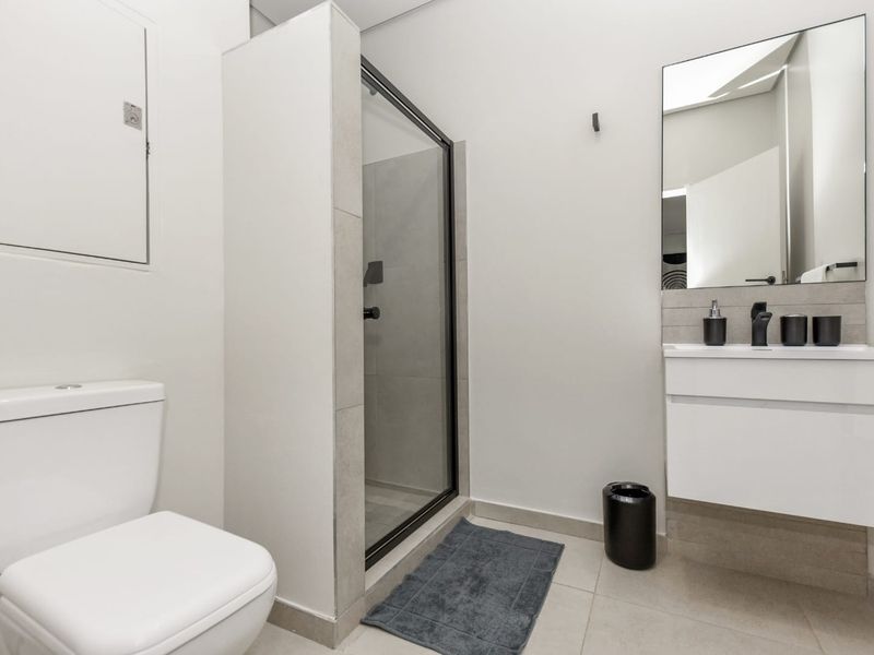 A modern, well-maintained bathroom featuring a glass-enclosed shower, a sleek white vanity with a basin, and contemporary black fixtures.