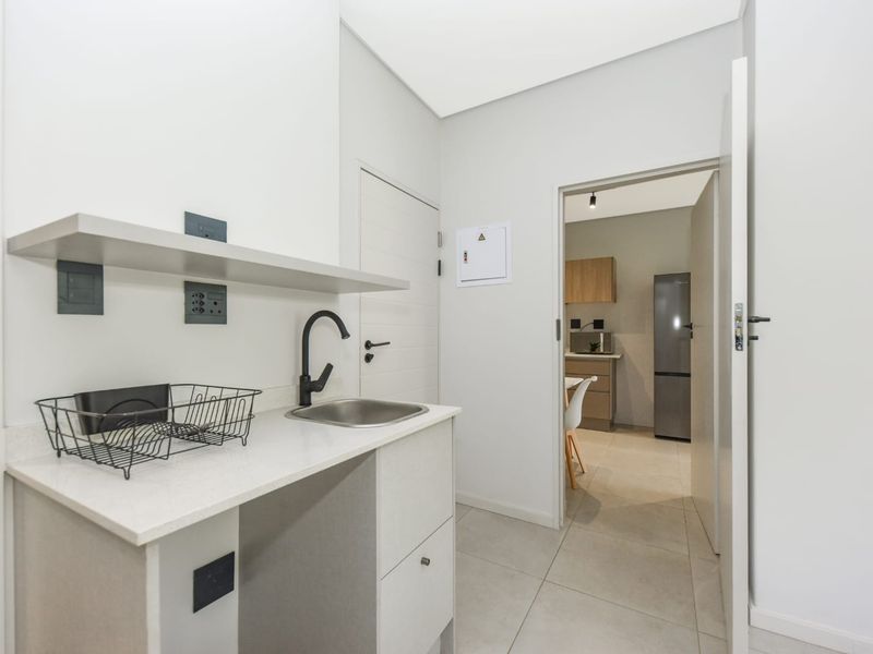 A clean and modern scullery area featuring a stainless steel sink, stone countertop, and built-in cabinetry with direct access to the kitchen.