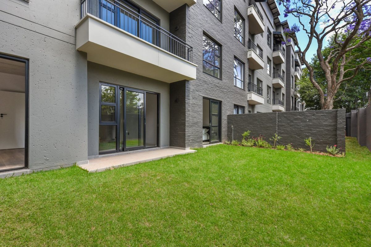 A modern apartment exterior featuring a private ground-floor patio, manicured lawn, and contemporary brick and plaster facade with sliding glass door access.