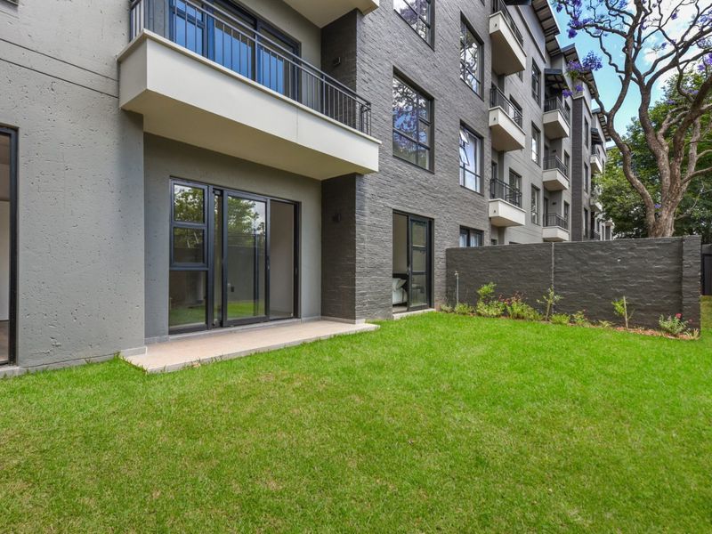 A modern apartment exterior featuring a private ground-floor patio, manicured lawn, and contemporary brick and plaster facade with sliding glass door access.