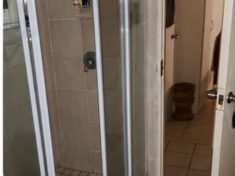 A functional bathroom featuring a corner shower enclosure with tiled walls and flooring, adjacent to a pedestal basin and doorway access.