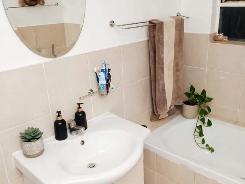 A functional bathroom featuring a vanity cabinet with a basin, a bathtub, and neutral wall tiling.
