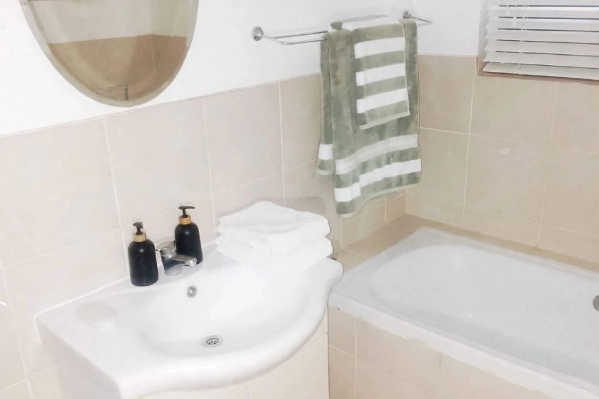 A functional bathroom featuring a vanity cabinet with a basin, a bathtub, neutral wall tiling, and venetian blinds for privacy.