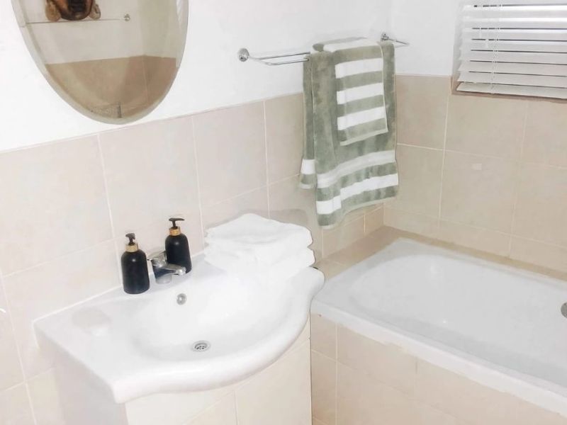 A functional bathroom featuring a vanity cabinet with a basin, a bathtub, neutral wall tiling, and venetian blinds for privacy.