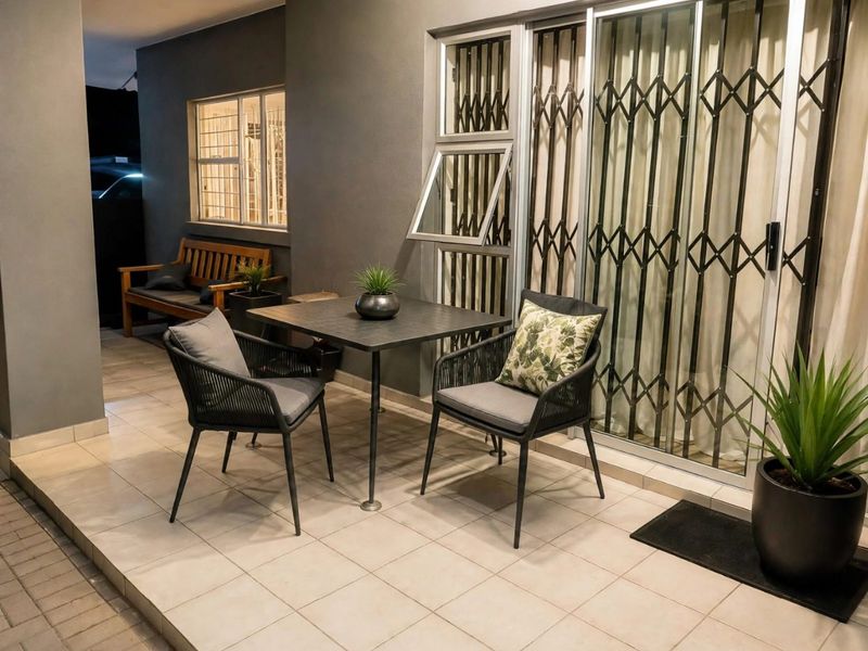 A covered patio area featuring tiled flooring, a sliding glass door with security gate, and a top-hung window.