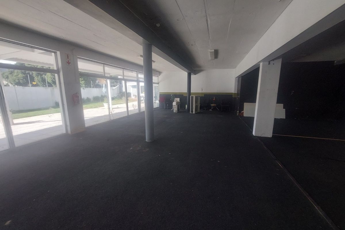 Spacious open-plan commercial area featuring large glass sliding doors, structural columns, and an exposed ceiling, offering a versatile layout for various business uses.