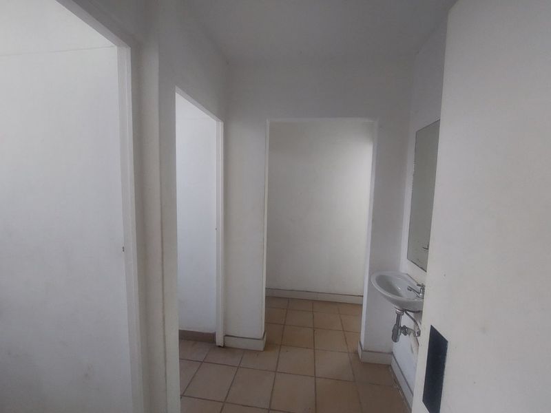 A simple, empty hallway area featuring tiled flooring and a wall-mounted basin with a mirror.