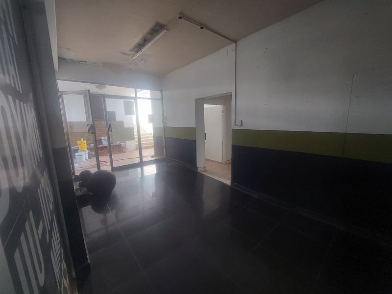 An empty commercial entry area featuring tiled flooring, glass sliding doors, and exposed ceiling lighting, currently requiring cosmetic updates.