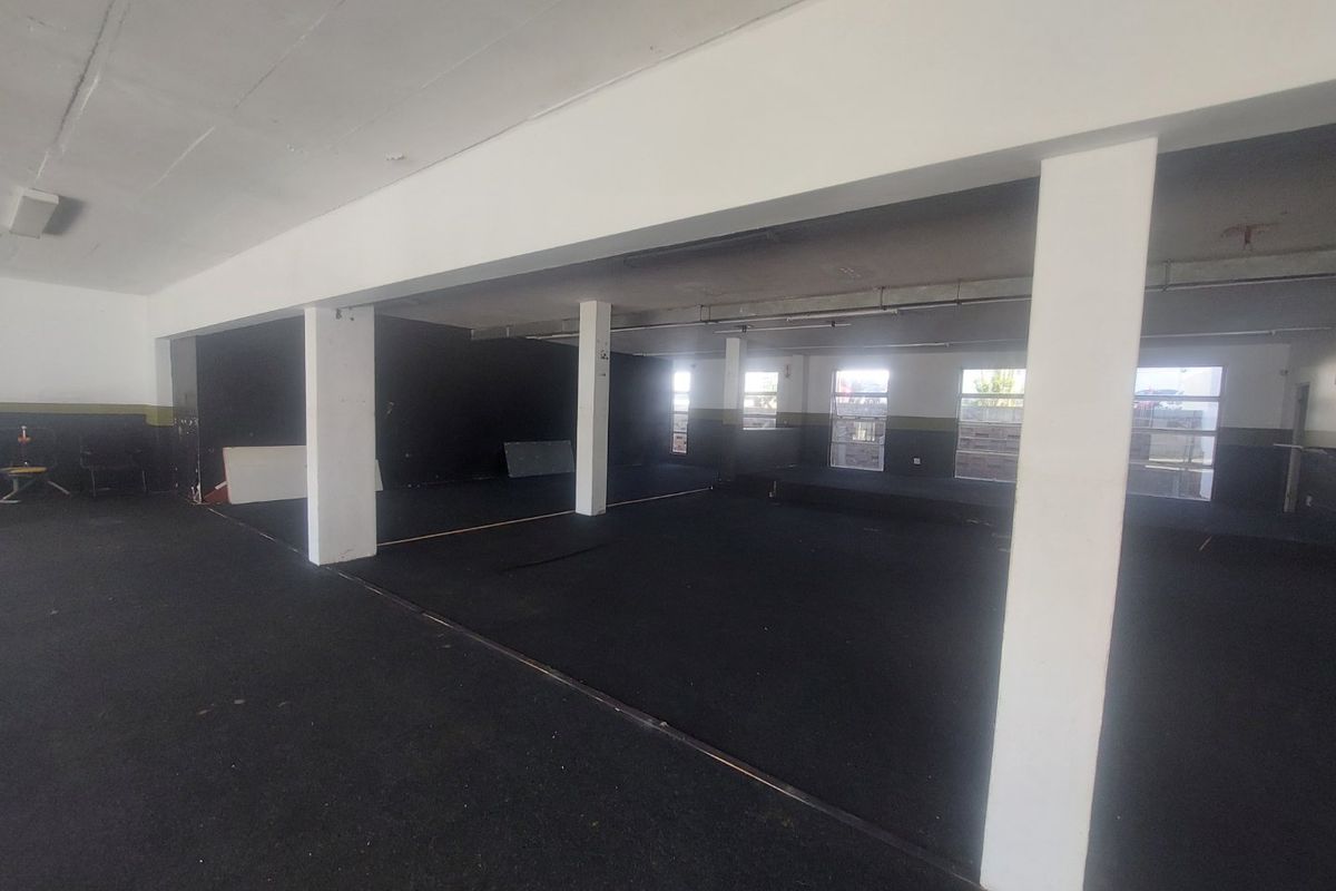 Spacious open-plan commercial area featuring structural columns, large windows for natural light, and durable rubberized flooring, suitable for various business applications.