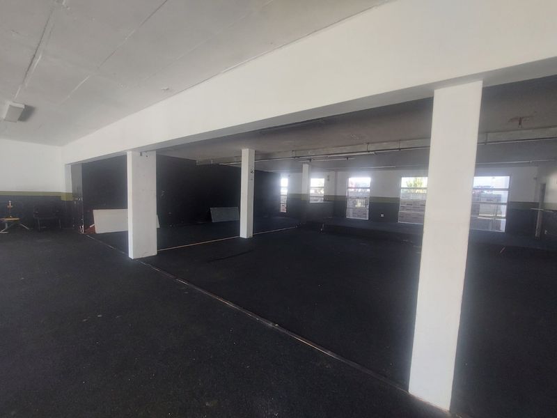 Spacious open-plan commercial area featuring structural columns, large windows for natural light, and durable rubberized flooring, suitable for various business applications.