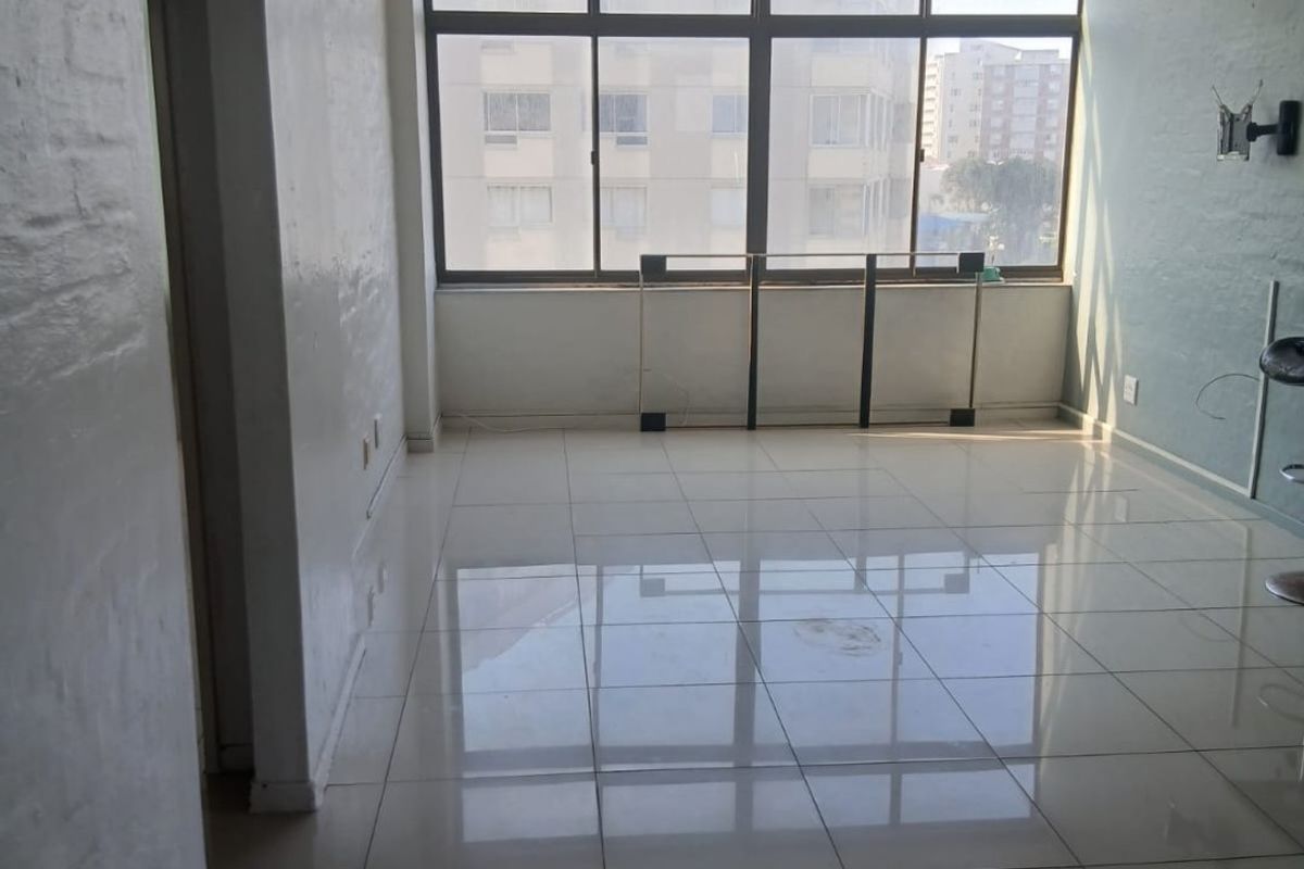A bright, empty living area featuring large windows, tiled flooring, and an arched entryway, offering a blank canvas for interior design.