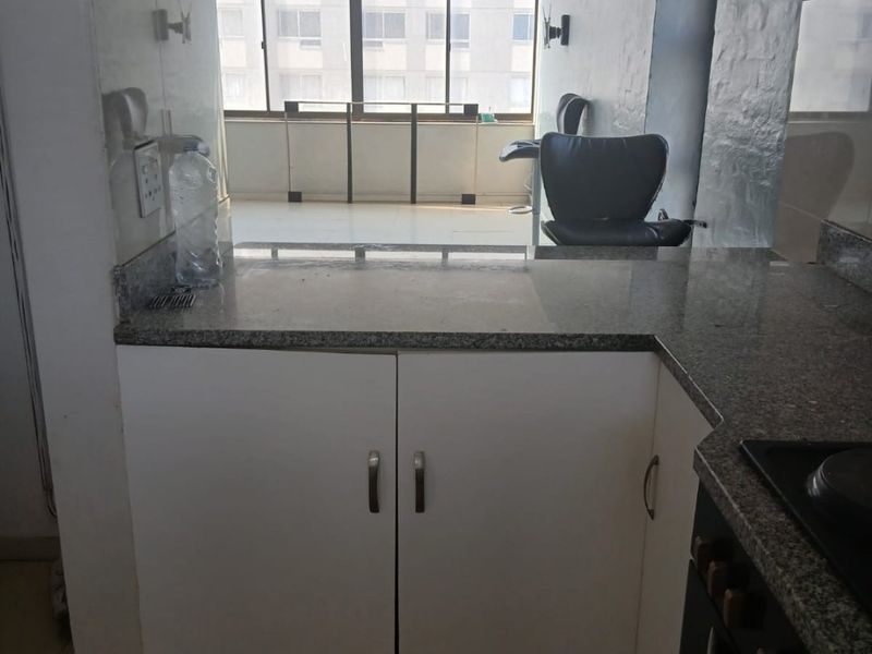 A functional kitchen area featuring granite countertops, built-in cabinetry, and an integrated oven and hob, with direct access to an adjacent living space.