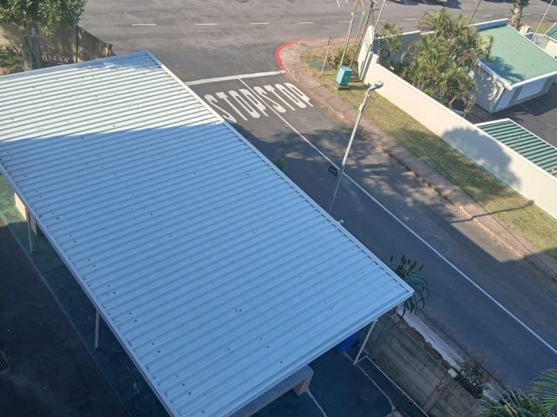 An elevated aerial view showing a residential carport, paved driveway, and surrounding street infrastructure.