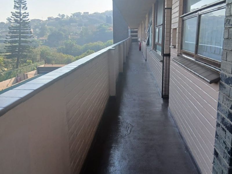 An exterior apartment balcony featuring a brick balustrade, tiled flooring, and metal window frames, offering an elevated view of the surrounding landscape.