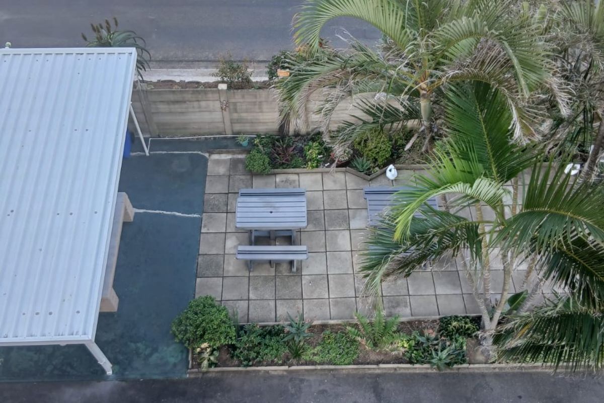 Aerial view of the property grounds featuring a paved patio area, metal carport, and established garden landscaping adjacent to the driveway.