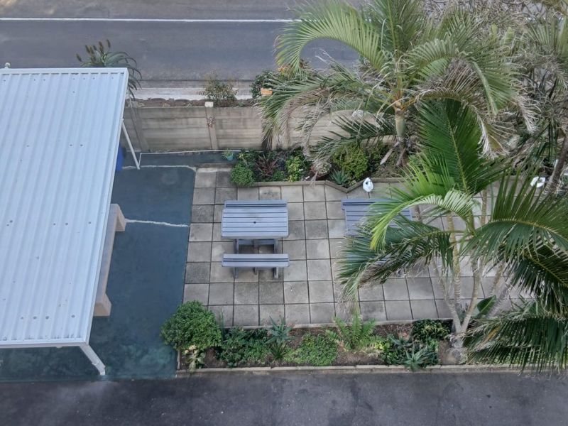 Aerial view of the property grounds featuring a paved patio area, metal carport, and established garden landscaping adjacent to the driveway.