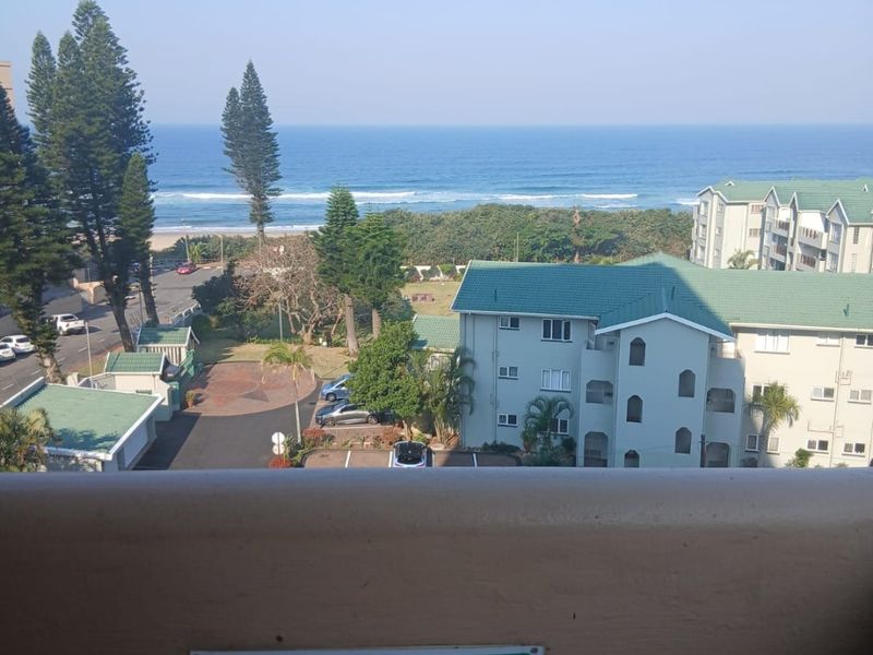 Elevated coastal view overlooking the ocean, surrounding apartment complex, and landscaped grounds from a balcony vantage point.