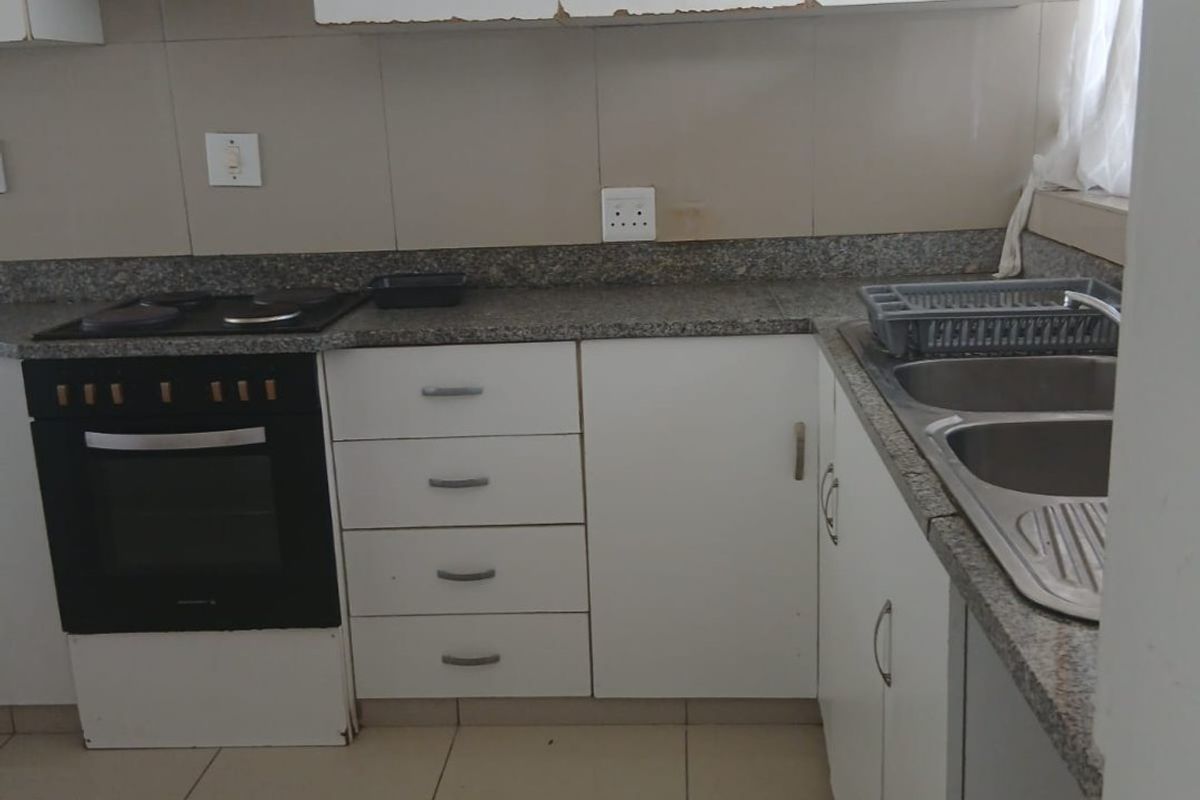 A functional kitchen featuring granite countertops, a built-in oven with hob, double stainless steel sink, and white cabinetry with tiled flooring and backsplash.