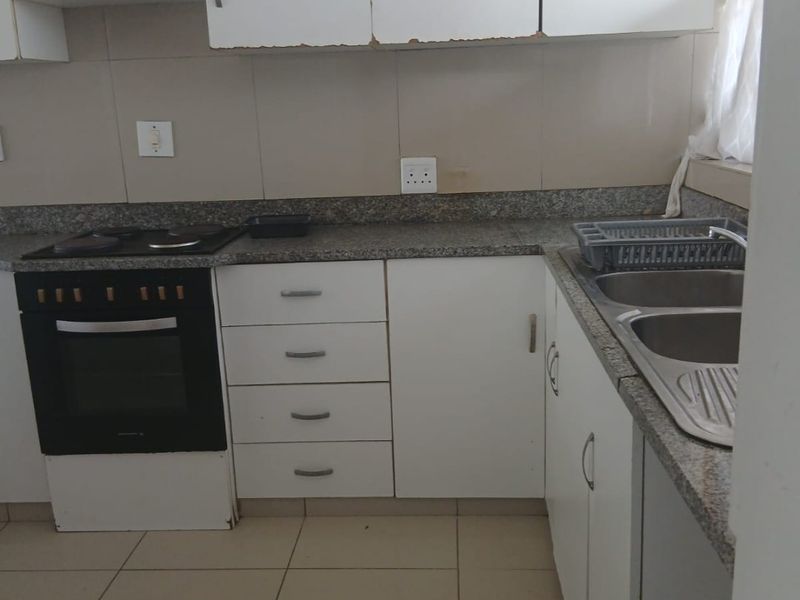 A functional kitchen featuring granite countertops, a built-in oven with hob, double stainless steel sink, and white cabinetry with tiled flooring and backsplash.