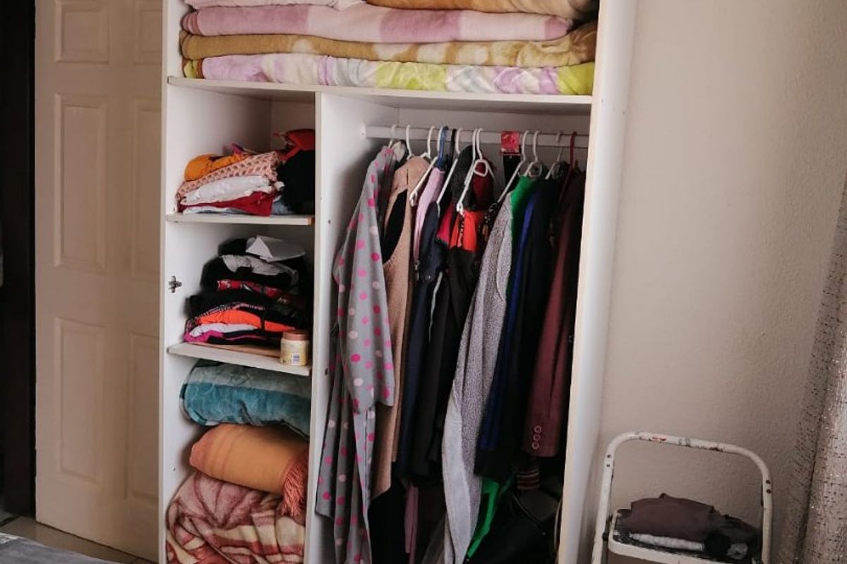 A bedroom featuring a white built-in wardrobe with shelving and hanging space for clothing storage.
