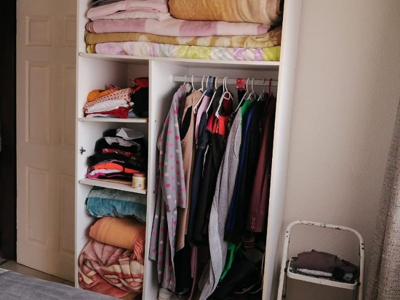 A bedroom featuring a white built-in wardrobe with shelving and hanging space for clothing storage.