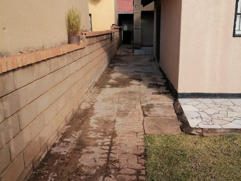 A narrow side passage featuring a paved walkway, boundary wall, and a small section of lawn alongside the house exterior.