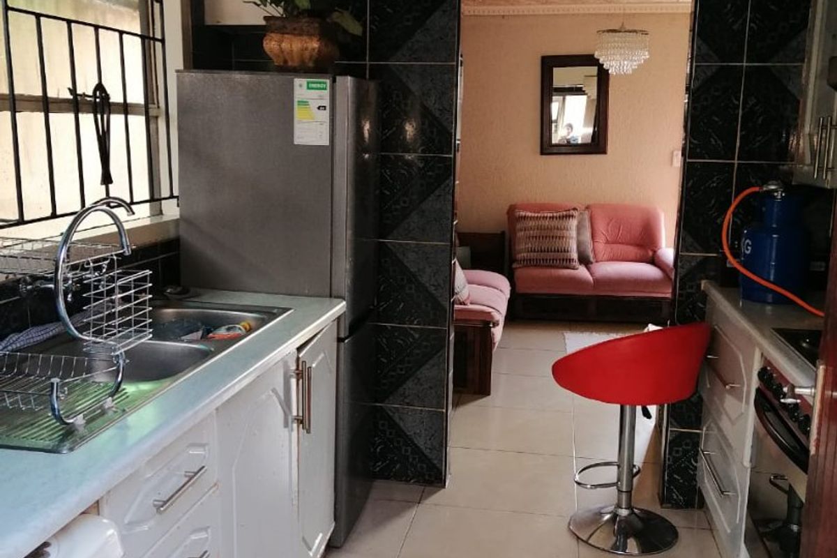 A compact kitchen featuring tiled walls, built-in cabinetry, and a double sink, with an adjacent view into the living area.
