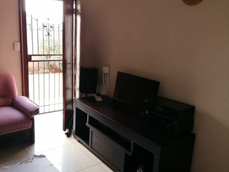 A living room area featuring tiled flooring, textured ceiling with molding, and a security gate leading to the exterior.