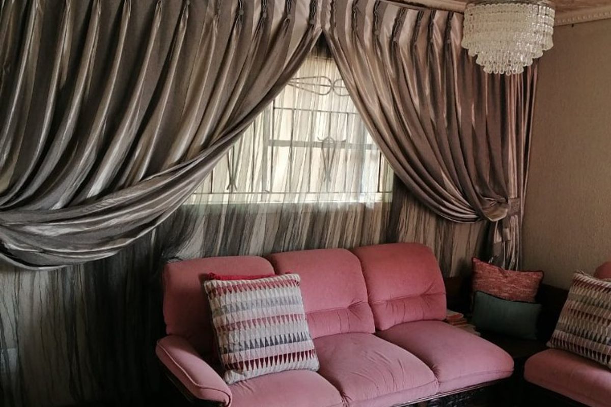 A living room featuring tiled flooring, a decorative ceiling rose, and textured ceiling tiles, with security bars installed on the window.