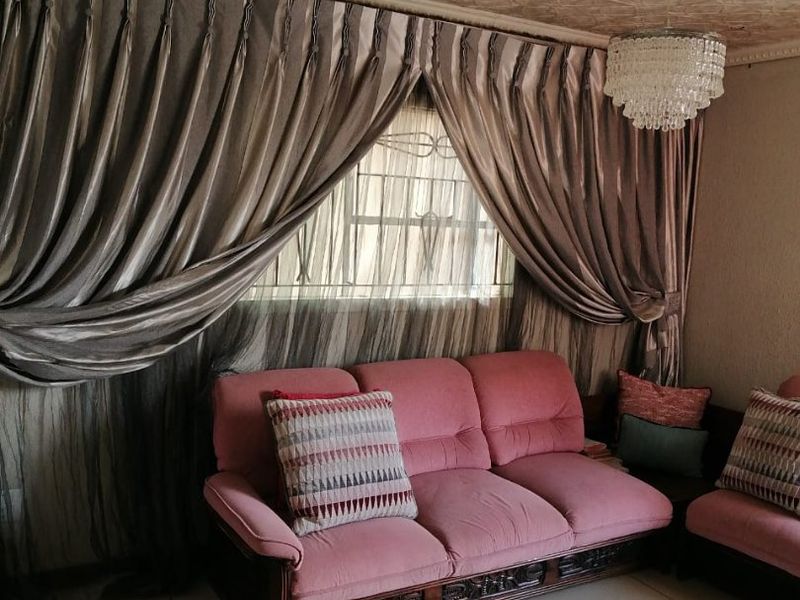 A living room featuring tiled flooring, a decorative ceiling rose, and textured ceiling tiles, with security bars installed on the window.
