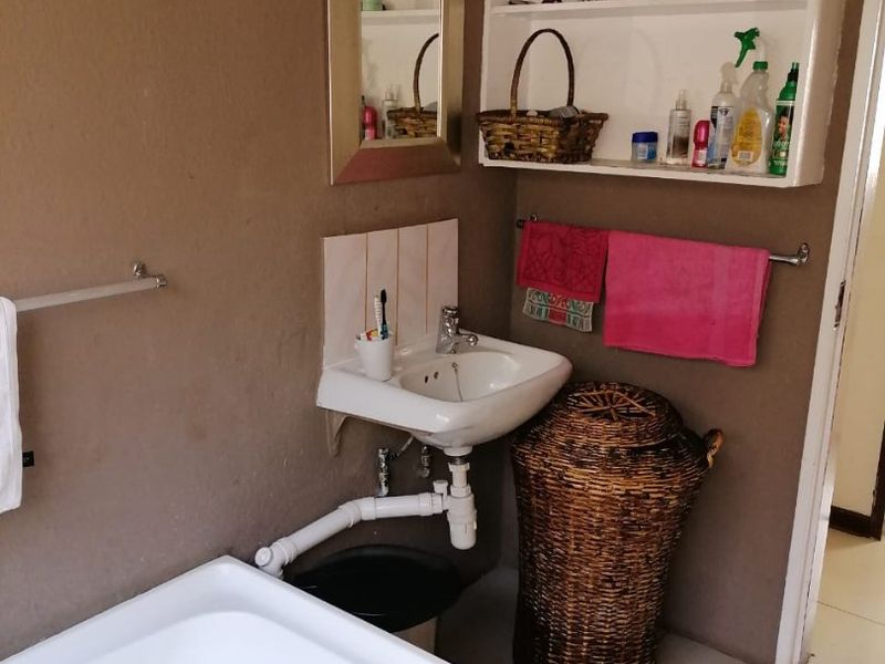 A compact bathroom featuring a wall-mounted basin with exposed plumbing, built-in wall shelving, and tiled splashback finishes.