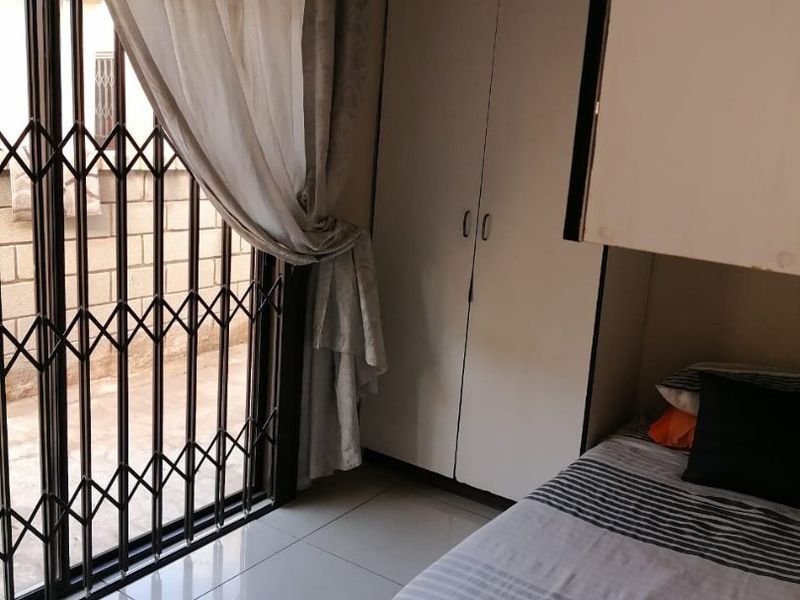 A bedroom featuring tiled flooring, a built-in wardrobe, and a sliding door with a security gate providing access to the exterior.