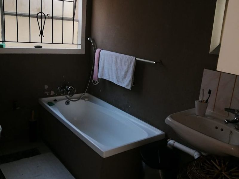 A compact bathroom featuring a bathtub, basin, and security bars on the window. The space requires cosmetic updates to improve its overall condition.