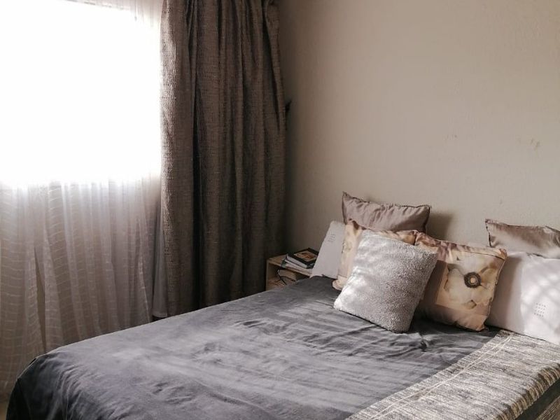 A functional bedroom featuring tiled flooring and a window with curtain treatments, providing a neutral space ready for personalization.
