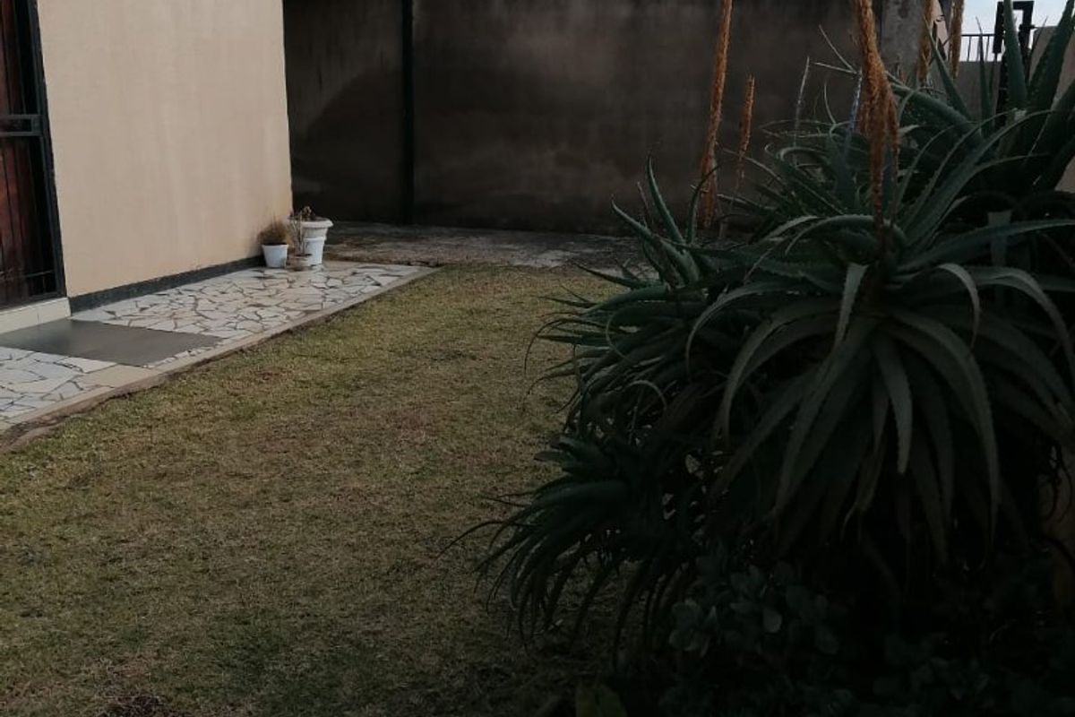 A rear garden area featuring a paved patio, lawn, and boundary wall with visible solar panels on the roof.