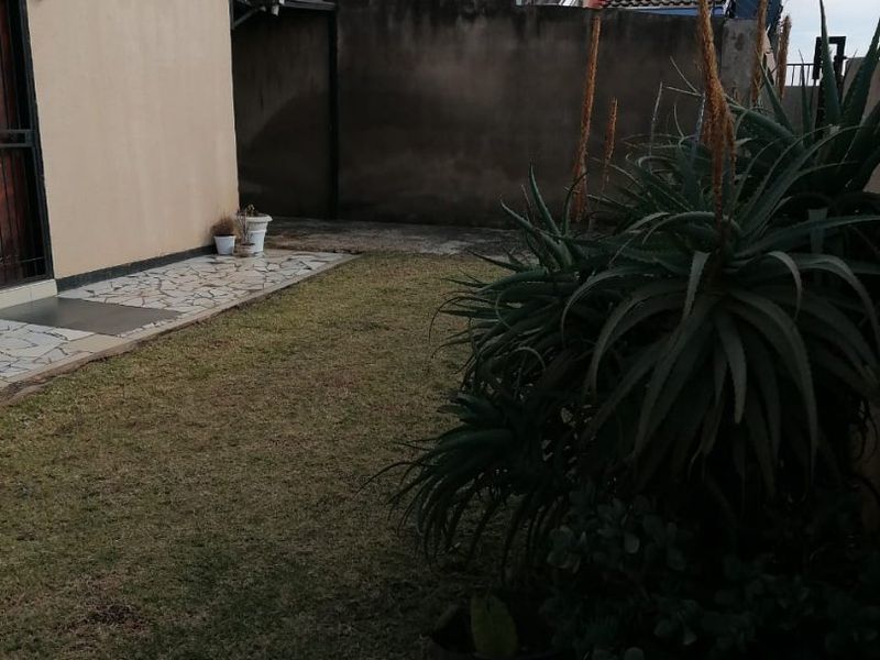 A rear garden area featuring a paved patio, lawn, and boundary wall with visible solar panels on the roof.