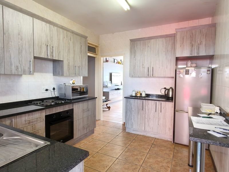 A functional kitchen featuring light wood-grain cabinetry, granite countertops, a built-in oven and hob, and tiled finishes throughout.
