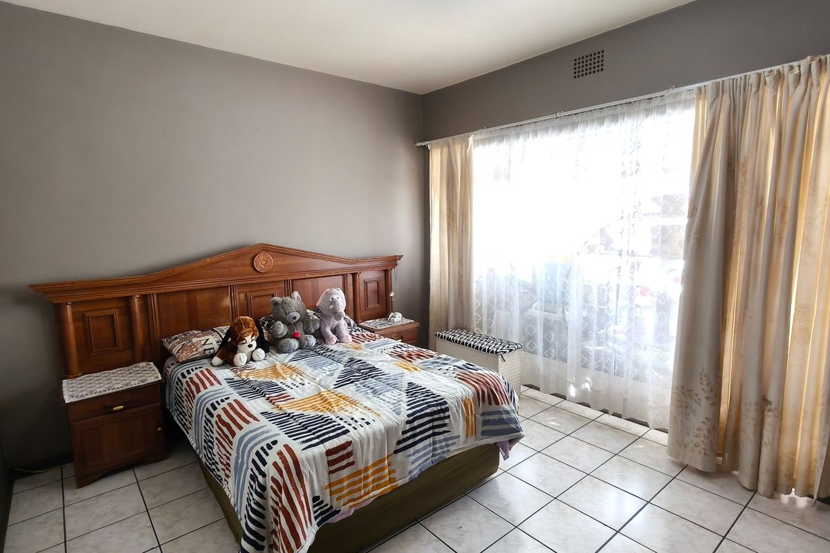 A bedroom featuring tiled flooring, a built-in wooden headboard with integrated bedside tables, and large windows with curtain tracks.