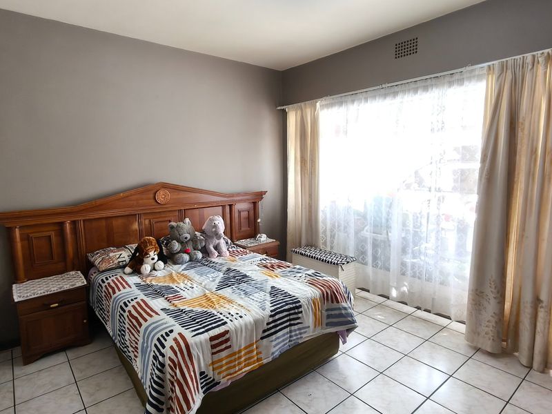 A bedroom featuring tiled flooring, a built-in wooden headboard with integrated bedside tables, and large windows with curtain tracks.