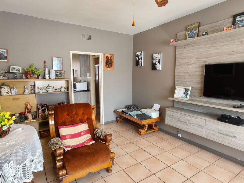 A living room featuring ceramic floor tiles, a built-in media unit, and a ceiling fan, with an adjacent view into the kitchen area.