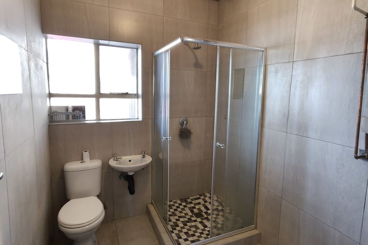 A functional bathroom featuring a shower enclosure, wall-mounted basin, toilet, and tiled finishes, with an exposed electric water heater.