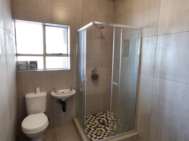 A functional bathroom featuring a shower enclosure, wall-mounted basin, toilet, and tiled finishes, with an exposed electric water heater.