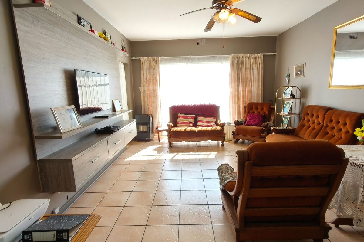 A spacious living room featuring tiled flooring, a ceiling fan, and a large built-in media console with integrated shelving.