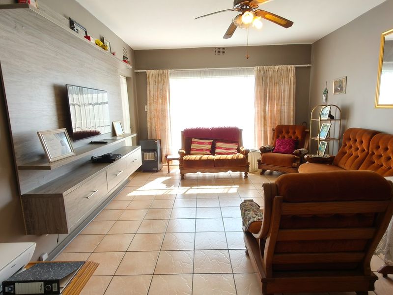 A spacious living room featuring tiled flooring, a ceiling fan, and a large built-in media console with integrated shelving.