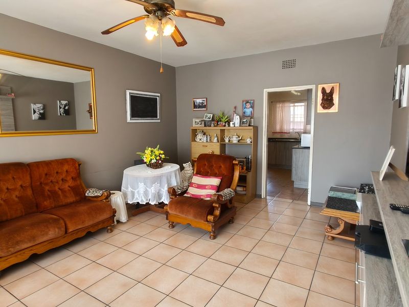 A living room featuring ceramic floor tiles and a ceiling fan, with an open doorway leading to the kitchen area.