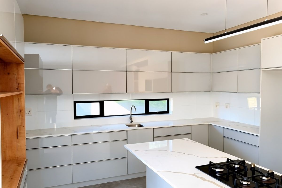Modern kitchen featuring sleek glossy cabinetry, stone countertops, a central island with a gas cooktop, and contemporary recessed and pendant lighting.