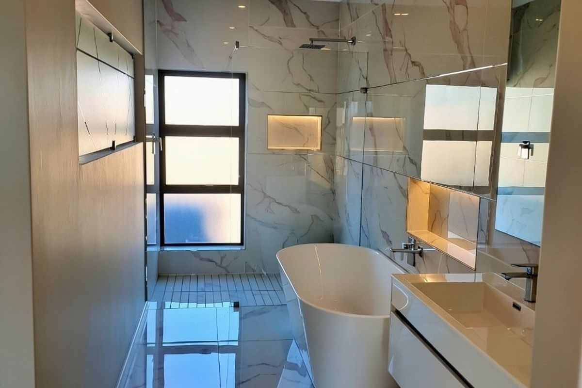 Modern bathroom featuring high-end marble-look tiling, a sleek freestanding bathtub, wall-mounted vanity, and a glass-enclosed shower area with recessed lighting.