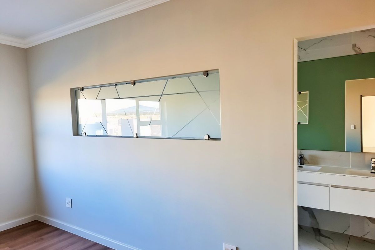 A clean, modern bedroom featuring laminate flooring, crown molding, and a unique decorative glass panel, with an open doorway leading to an en-suite bathroom.